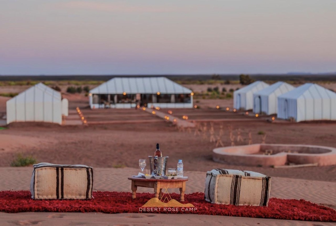 Rincón con pufs y alfombra roja frente al campamento al atardecer