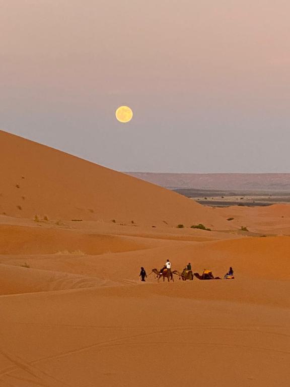 Luna llena sobre las dunas con un grupo de camellos al atardecer
